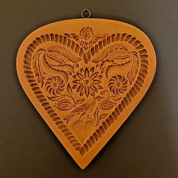 Decorative heart-shaped wall hanging with floral and leaf patterns on a brown background